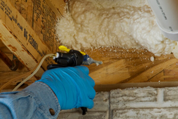 person spraying foam around pipe